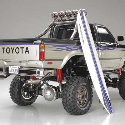 TAMIYA TMYTAM58397 1:10 RC Toyota HiLux HighLift 4x4 3-Gang - ferngesteuertes Auto - inkl. Surfbrett