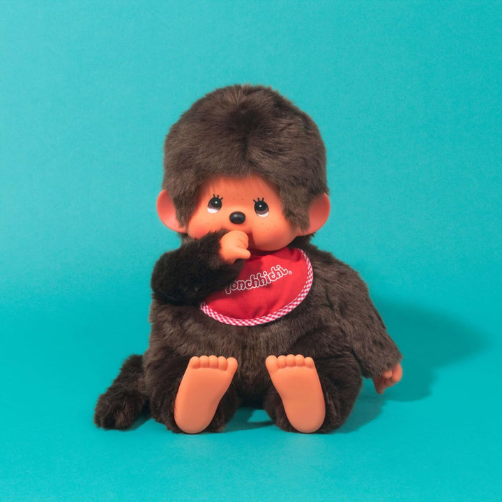 Sekiguchi 255410 - Original Monchhichi Junge, Plüschtier mit rotem Lätzchen und Zöpfen mit Schleifen